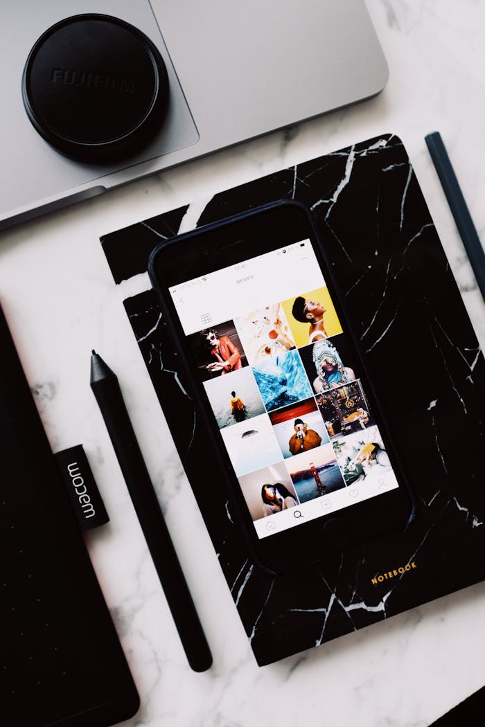 Black organizer with mobile phone app demonstrating creative images on screen and cup located on laptop touch pad near marker put on marble table